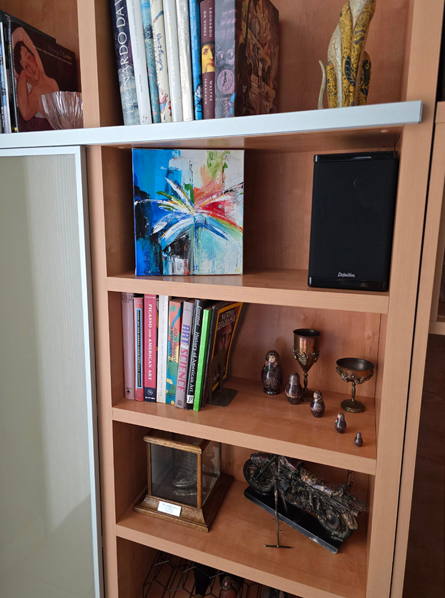 Wooden bookshelf with books and decorative items against a neutral wall showcasing the abstract palm painting.