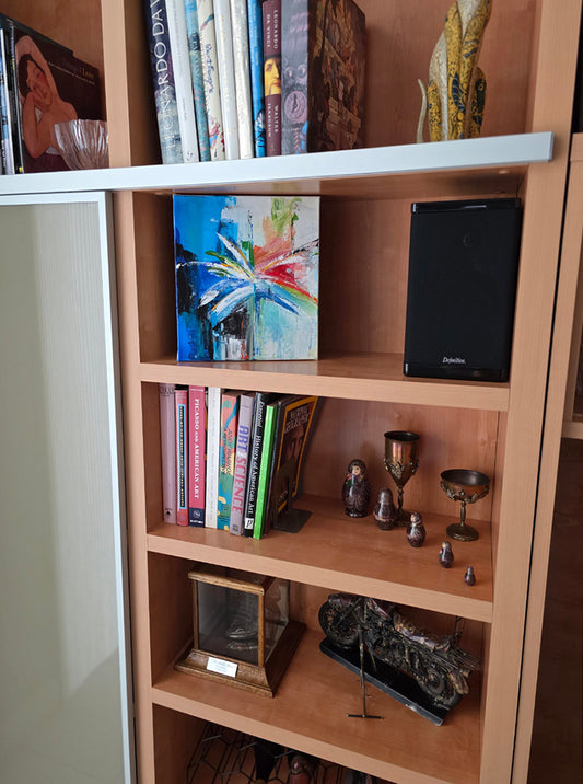 Wooden bookshelf with books and decorative items against a neutral wall showcasing the abstract palm painting.