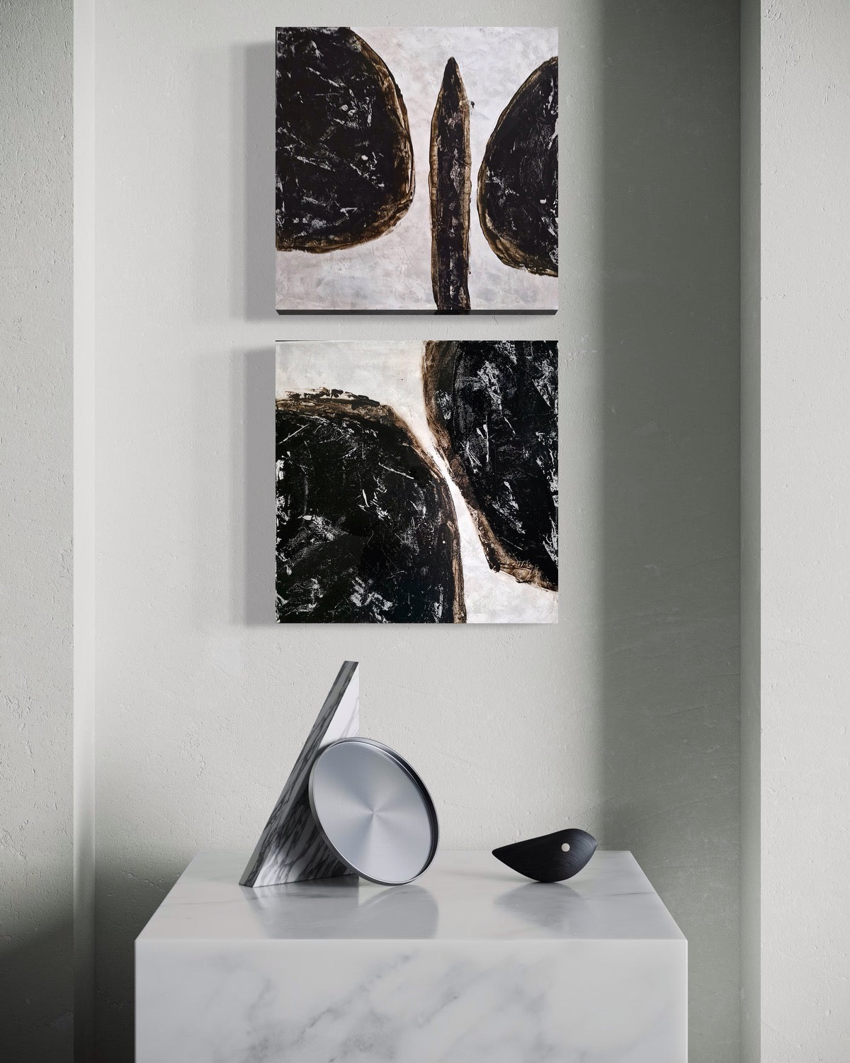 Two abstract art black and white paintings against white background above a stand with decorative objects