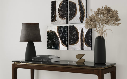 Decorative table with a lamp, books, and vase against a wall with abstract art.