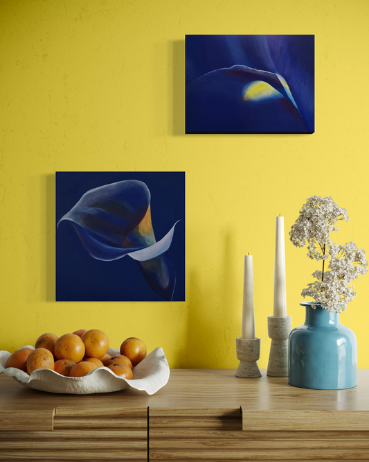 Two abstract paintings of flowers on a yellow wall above a wooden table with decorative items.